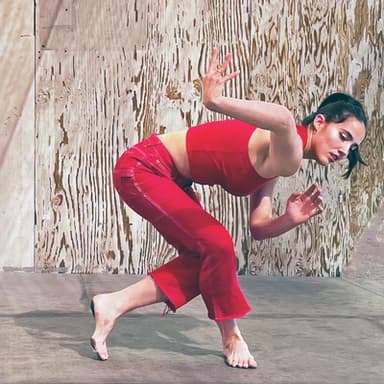 Alex Carrington, wearing red, curls and twists her arms and legs.