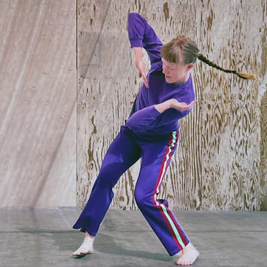 Chelsea Reichert, wearing purple, twists her arms and torso while her braid swings out to the opposite side.