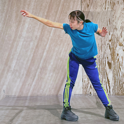 Mia J. Chong, wearing shades of blue, bands over straight legs and reaches one arm straight to the side.